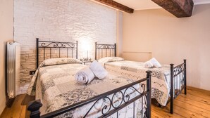 Ein Doppelbett mit gemustertem Überwurf und zwei Kissen, eine Heizung und eine Steinwand.