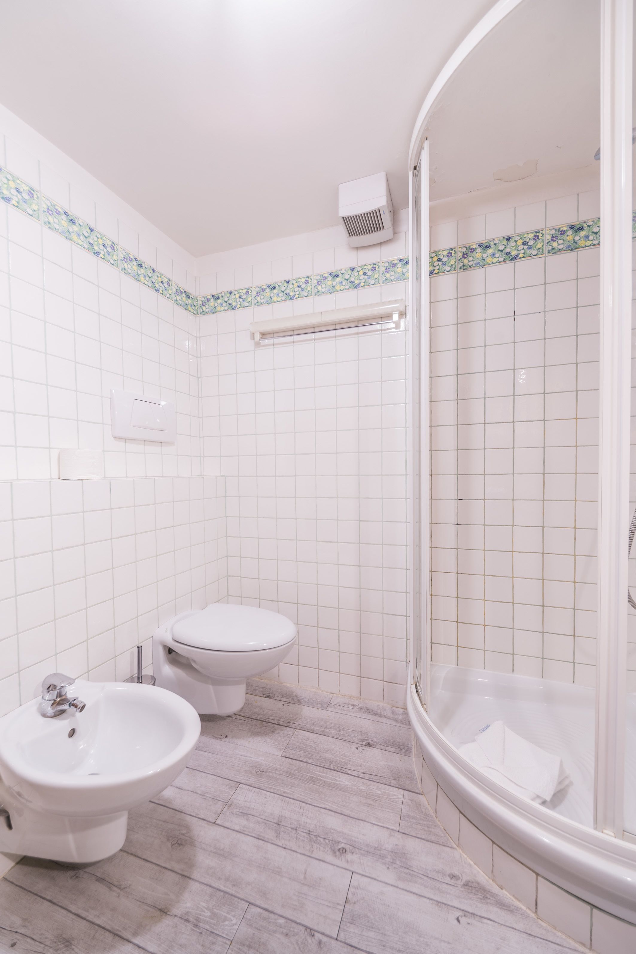 A bathroom with white tiles, a shower, a bidet, and a bathtub.