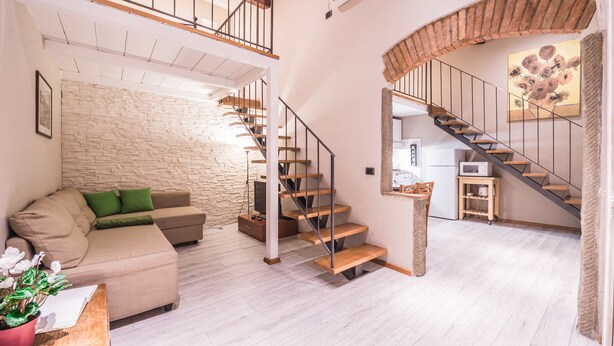 Ein geräumiger Wohnbereich mit einer Holztreppe, einer Steinwand und einer modernen Küche im Hintergrund.