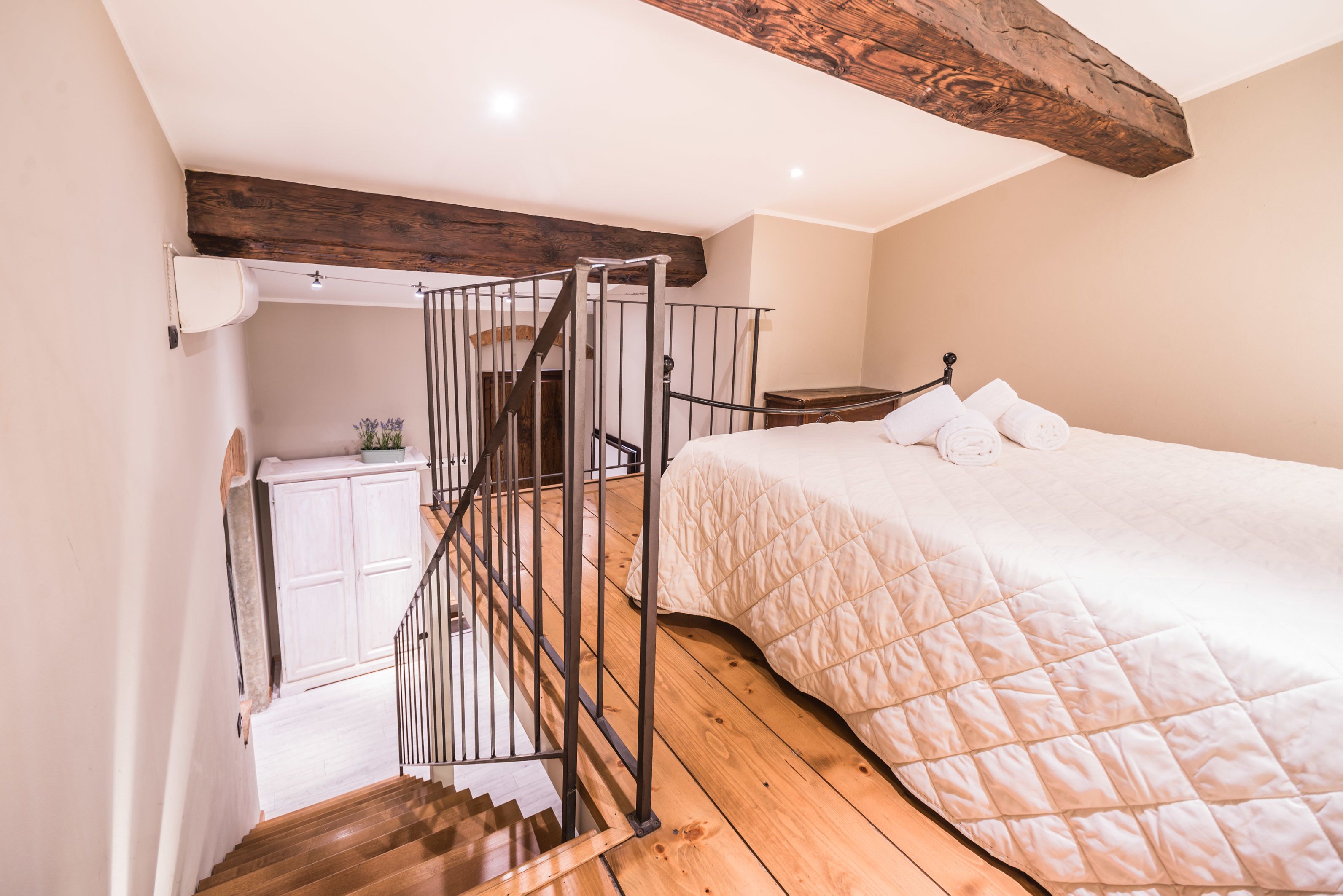 A bedroom with a wooden staircase, a bed with a quilted duvet, and a nightstand.
