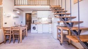 Eine kleine Küche mit Waschmaschine, ein Essbereich mit Holzmöbeln und eine Treppe mit Metallgeländer.