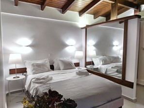 A hotel room with a large bed, two bedside tables, a mirror, and a ceiling with wooden beams. - Vivo Apartments (Marousi)