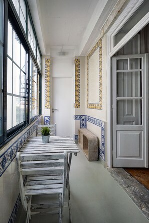 A narrow hallway with a white door, a bench, and a small table with a potted plant. - 1924 (Lisbon)
