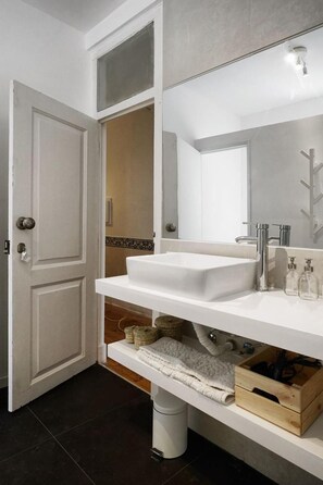 A bathroom with a white sink, mirror, and towel rack. There is a door with a keyhole and a small trash bin under the sink. - 1924 (Lisbon)