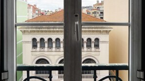 A view through a window with a metal railing, featuring a building with arched windows and a tiled roof. - 1924 (Lisbon)