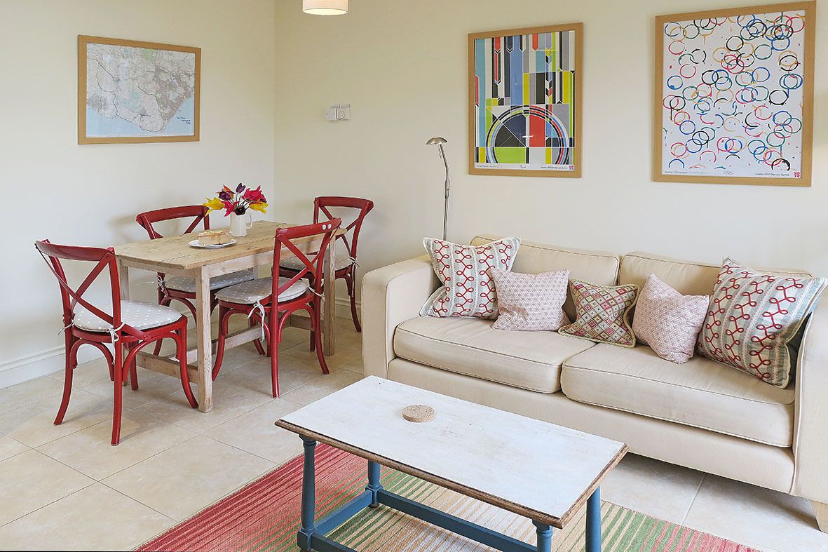 A living room with a beige sofa, red chairs, a wooden dining table, and a white coffee table.