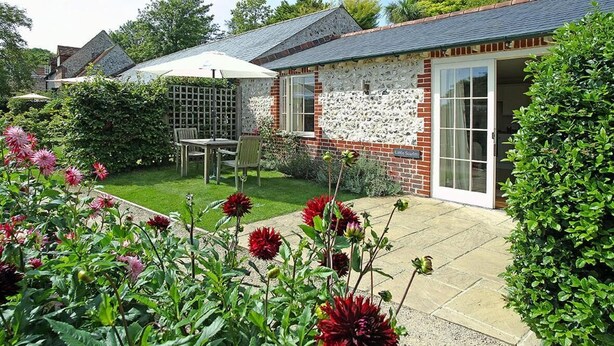 Une maison en briques avec un jardin, une terrasse avec une table et des chaises, et un espace abrité avec un parasol blanc.