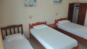A room with three wooden beds, each with white bedding. There are wall-mounted light fixtures and a wardrobe. - Alexandros Guest House (Skiathos)