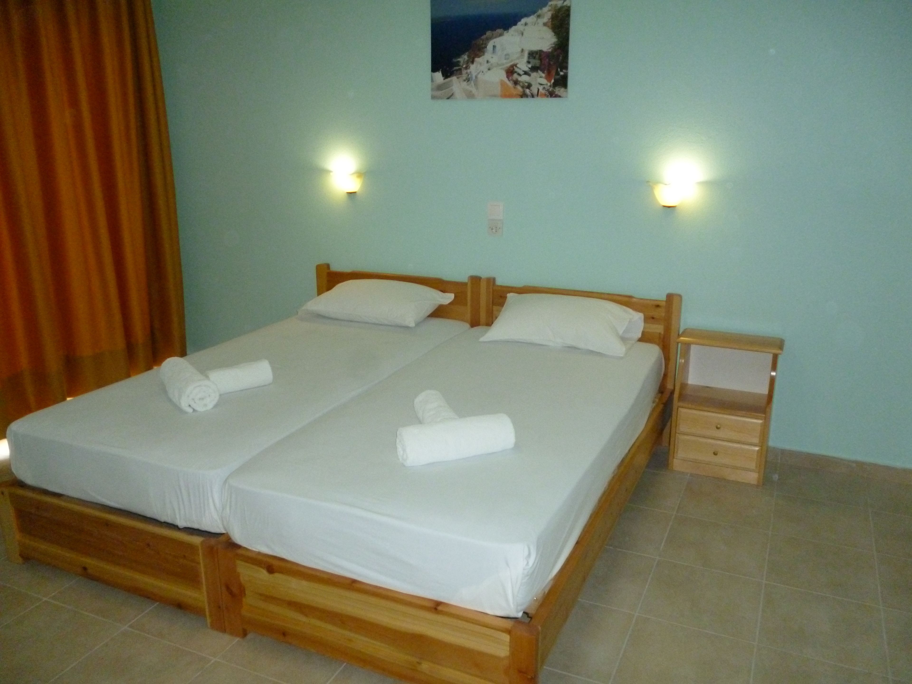 Cama doble con dos almohadas y mesita de noche de madera con cajón.