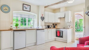 A modern kitchen with white cabinets, a dishwasher, a stove, and a window with a view of greenery. - Beachy Barn (Eastbourne)