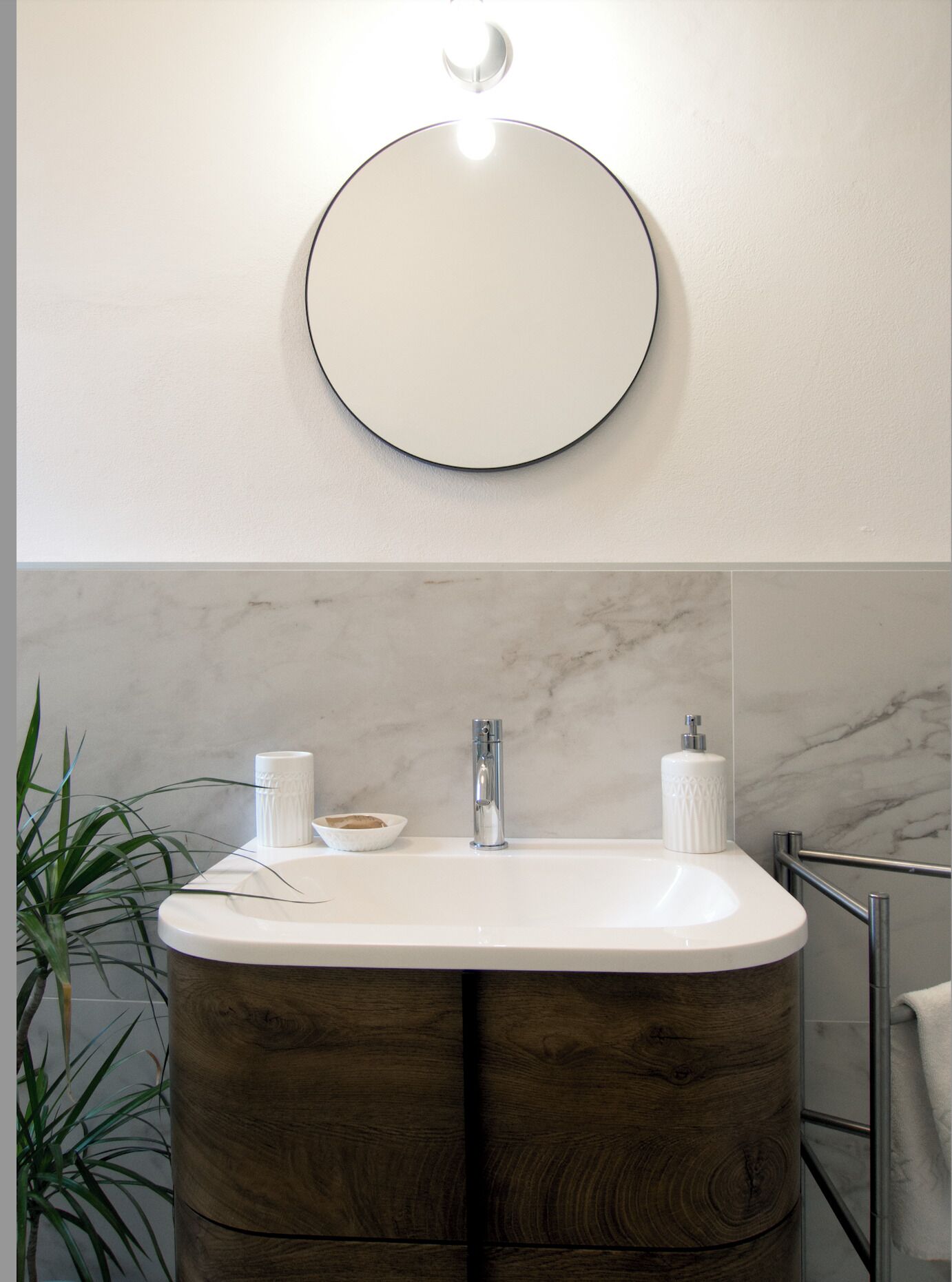 A bathroom with a round mirror, a white sink, and a wooden vanity.
