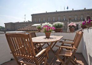 A wooden table and chairs on a terrace with potted flowers and a building in the background. - Best Location Rooftop and Pitti Palace View (Florence)