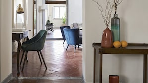 A spacious hallway with a high ceiling, a dining area with blue chairs, and a table with a vase and oranges. - Best Location Rooftop and Pitti Palace View (Florence)