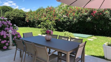 En udendørs terrasse med et bord og stole, omgivet af frodigt grønt og blomstrende planter.