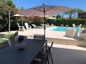 A pool area with lounge chairs, a table with a vase of flowers, and a large umbrella. - Bed & Breakfast da Beatrice (Sirmione)