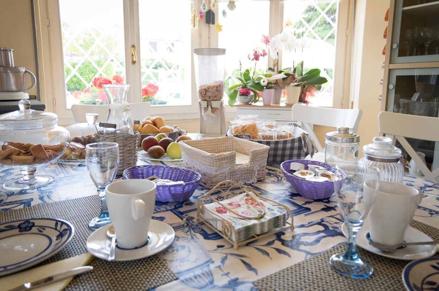 Et morgenbord dækket med tallerkener, kurve og glas, med udsigt til en have gennem et vindue.