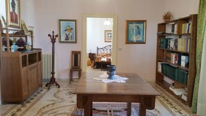 A hallway with a wooden table, a radiator, a chair, a bookshelf, and framed pictures on the walls. - B&B Casa Resci (Tricase)