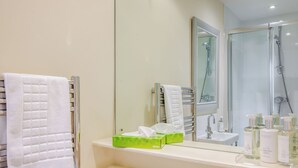 Een badkamer met een douchecabine van glas, een witte wastafel en een spiegel boven de wastafel.