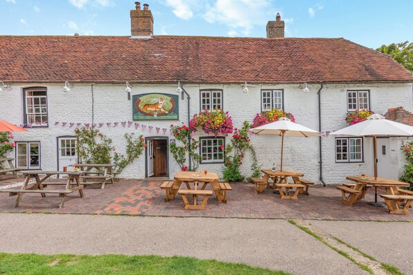 A white building with a red-tiled roof, wooden picnic tables, and flower boxes.