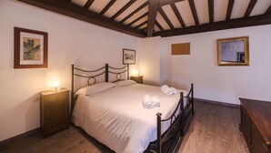 Ein Schlafzimmer mit Holzboden, einem Bett mit weißen Leinen, zwei Nachttischen mit Lampen und gerahmten Bildern an den Wänden.