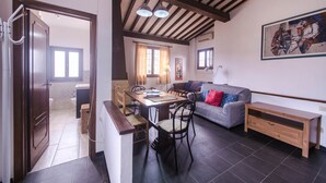 Ein geräumiger Wohnbereich mit einem Holzessttisch, einer Couch und einer Bank. Im Hintergrund befindet sich eine Küche mit einem Fenster und einer Tür zu einem anderen Raum.