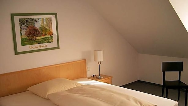 Un lit simple avec une tête de lit en bois, une table de chevet avec une lampe et un tableau encadré au mur.
