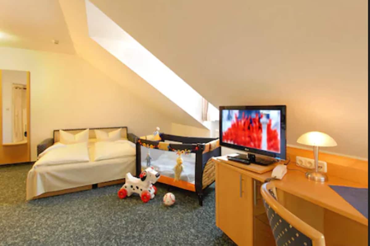 A hotel room with a bed, a desk with a computer, a television, and a lamp.