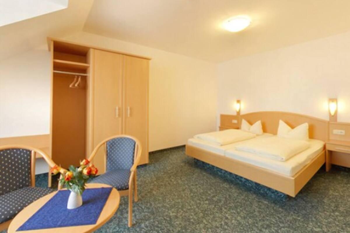 A hotel room with a bed, a chair, a table, and a wardrobe.