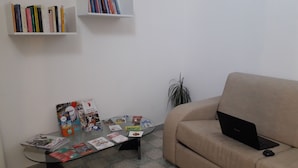 Ein Wohnzimmer mit einem Glastisch, einem beigefarbenen Sofa, einem Laptop und Bücherregalen an der Wand.