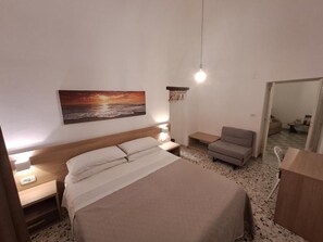 Un dormitorio con cama, mesita de noche, lámpara y un cuadro de un atardecer.