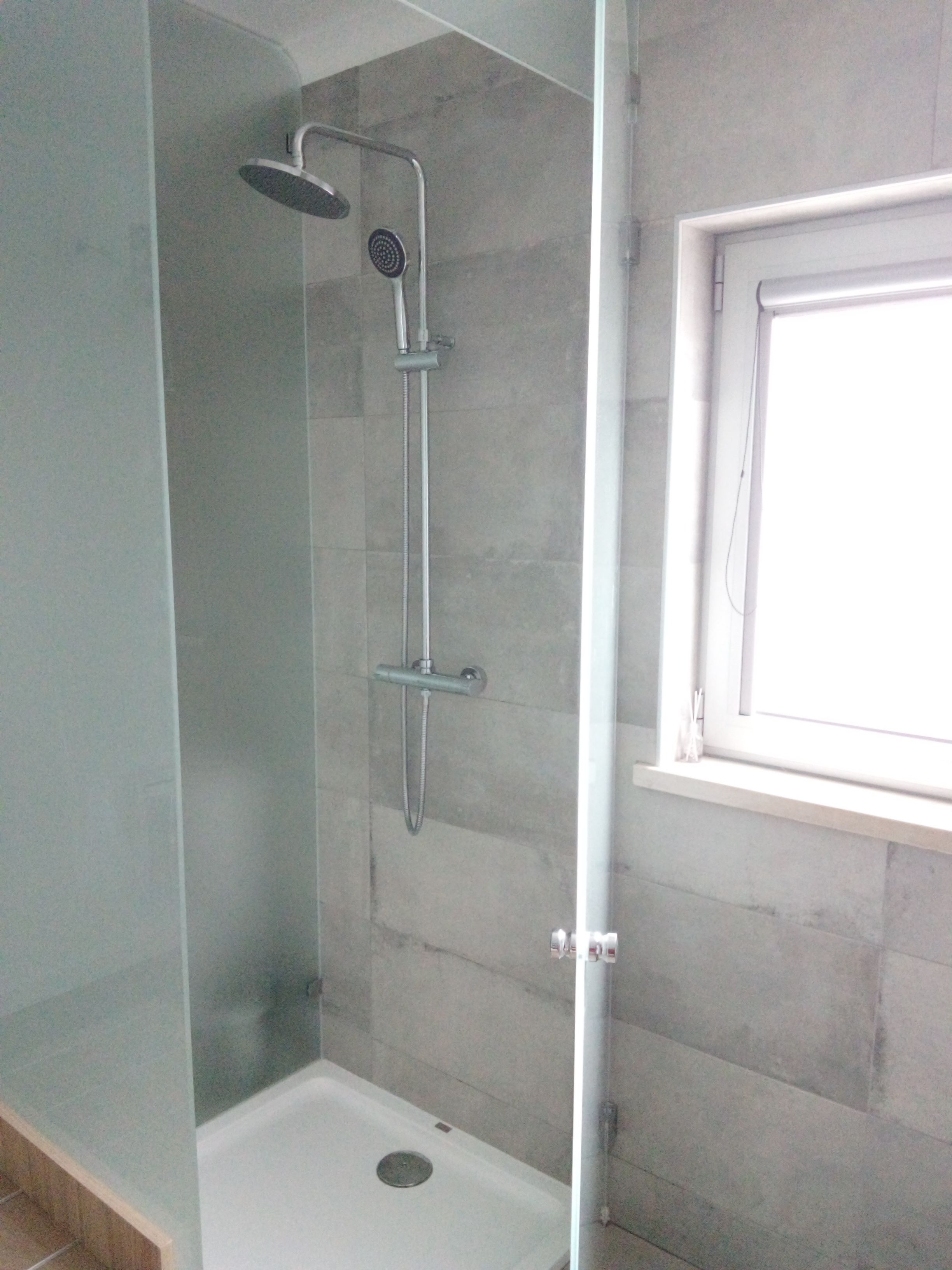 A glass-enclosed shower with a handheld showerhead and a wall-mounted faucet.