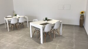 Un espace repas moderne avec des tables et des chaises blanches, une plante en pot et un vase en bois contenant un tournesol.