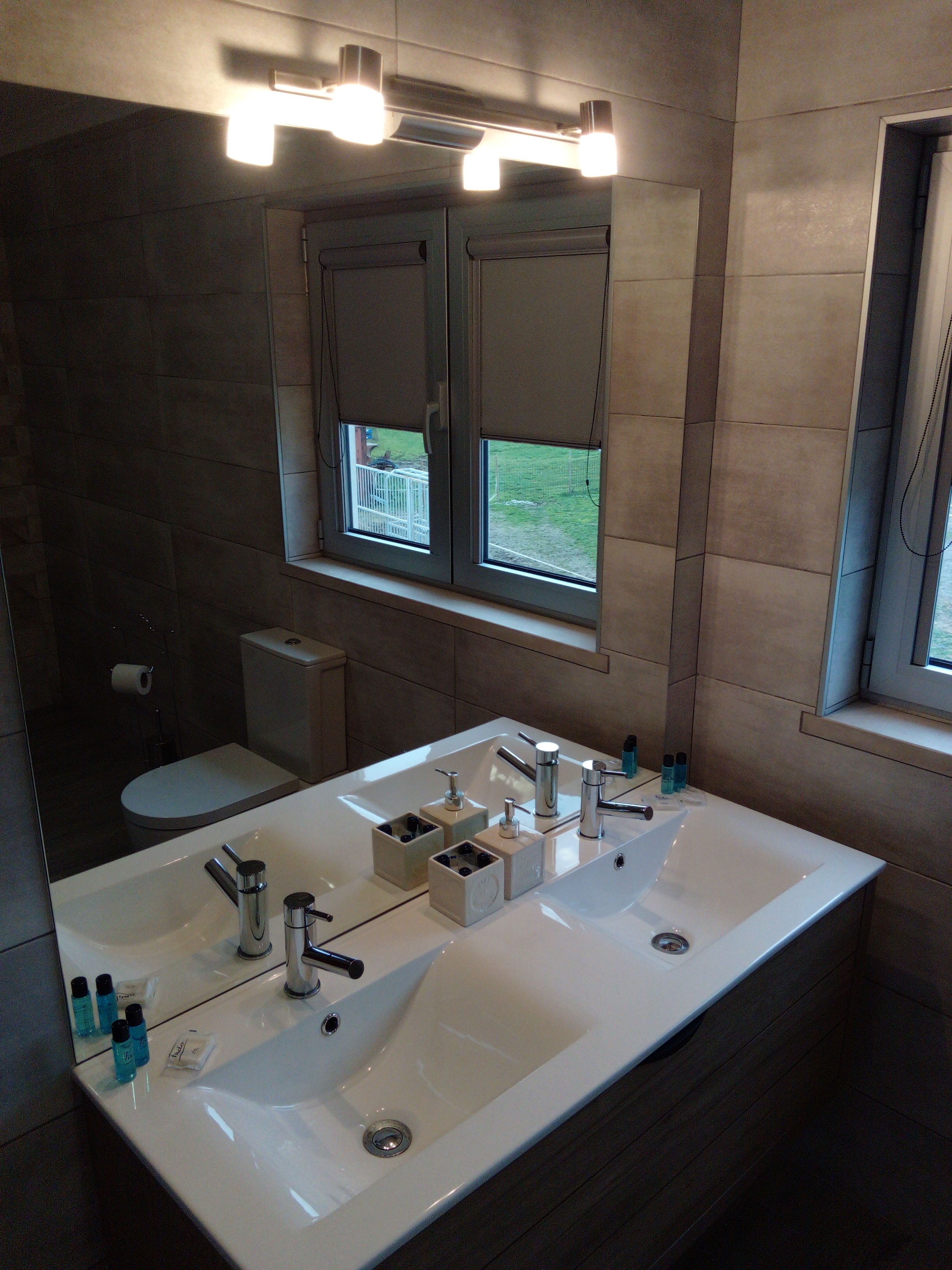 A modern bathroom with a large white sink, two mirrors, and a window with a view of the outdoors.