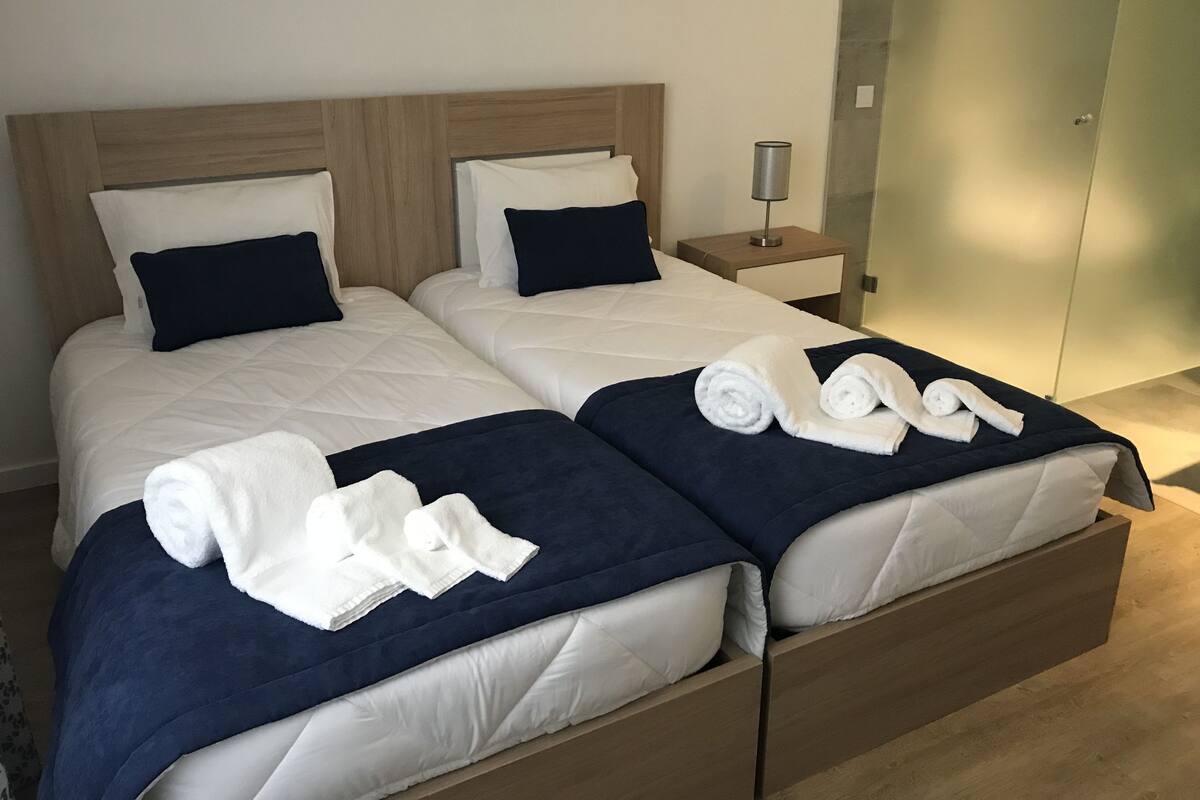 A double bed with white and navy bedding, a wooden headboard, and a nightstand with a lamp.