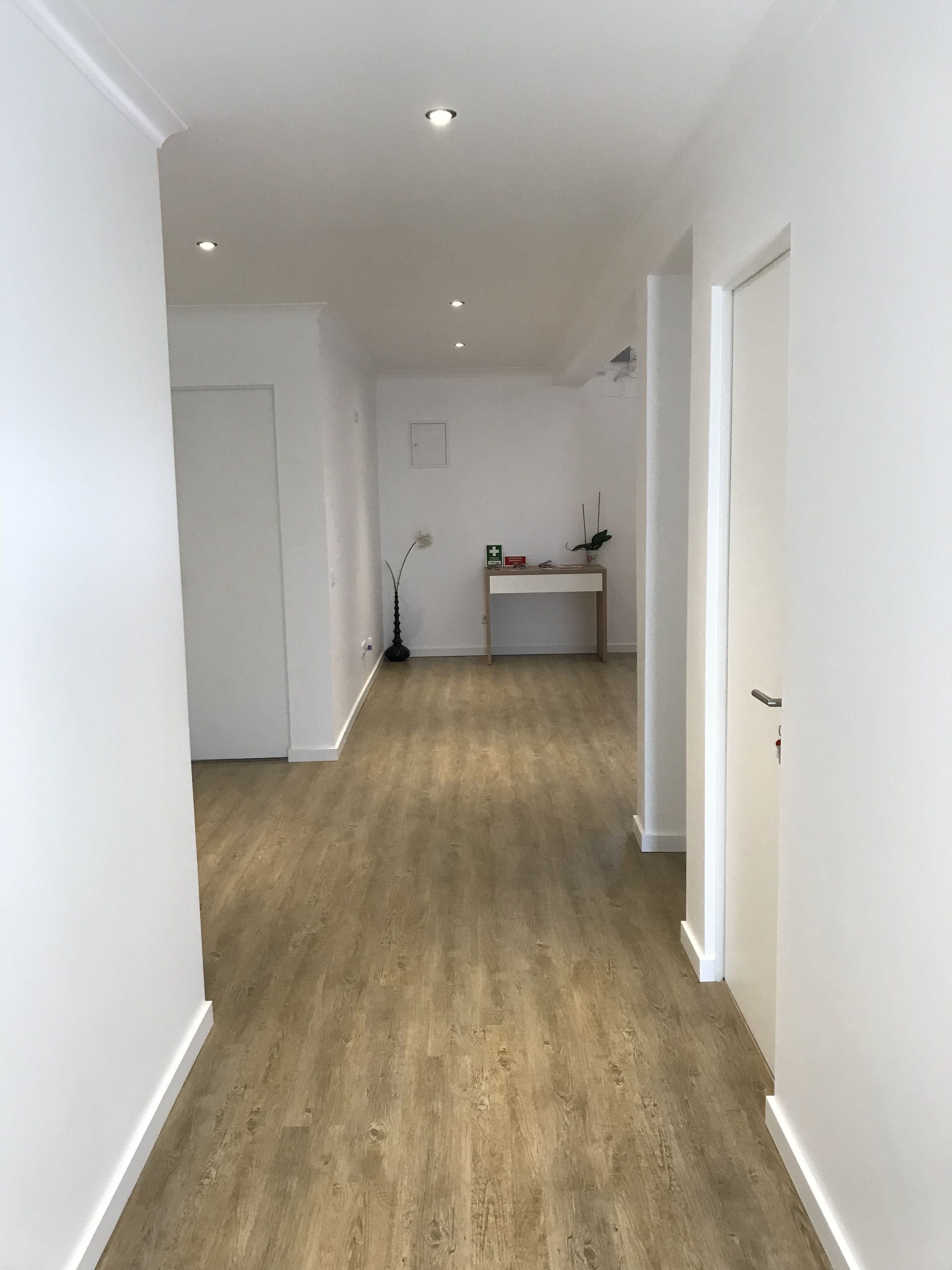 Un corridoio con pavimento in legno, pareti bianche e luci a incasso nel soffitto.