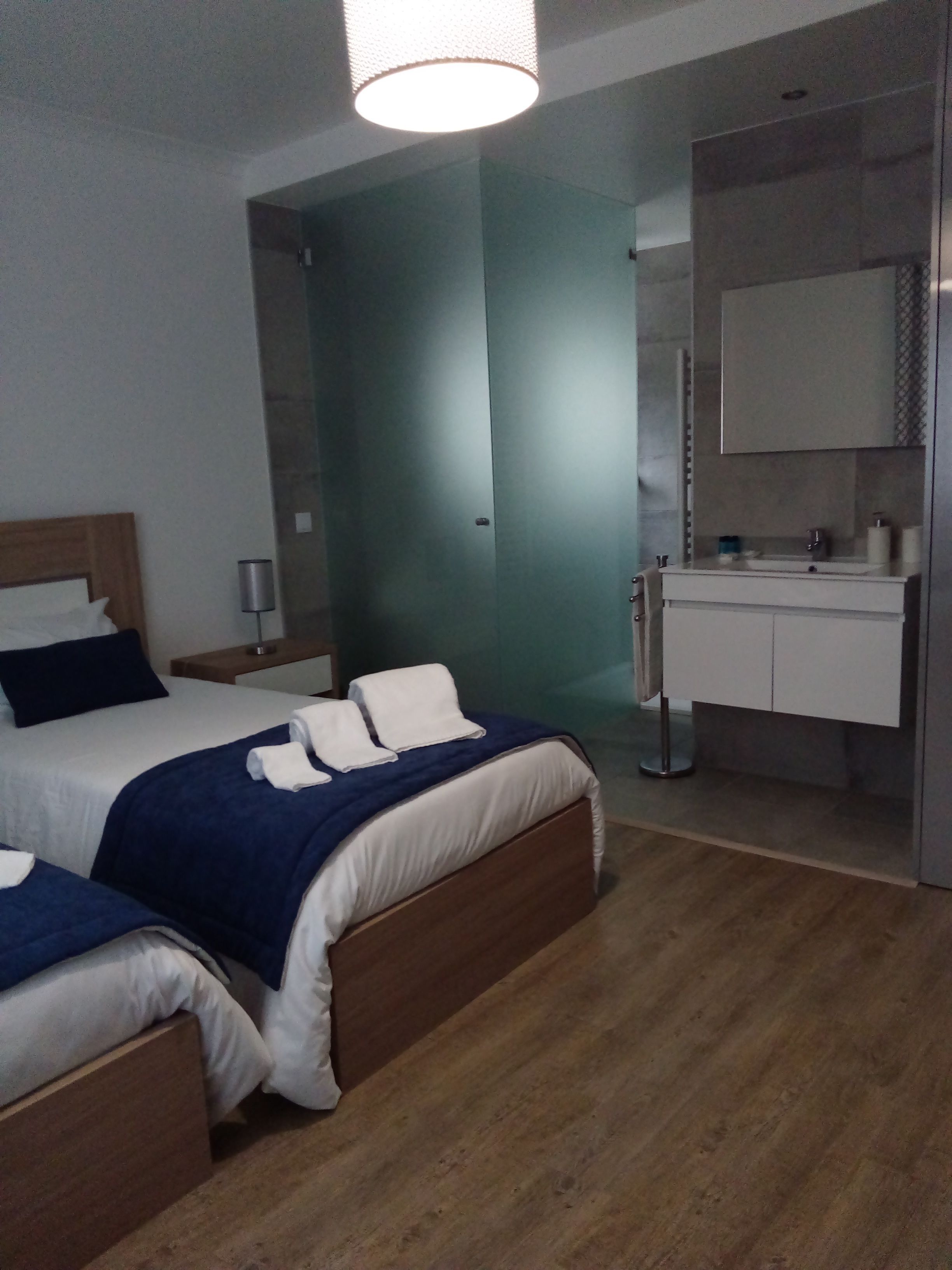 Une chambre d’hôtel avec un grand lit, une table de chevet, une lampe, une salle de bain avec un miroir et un lavabo.