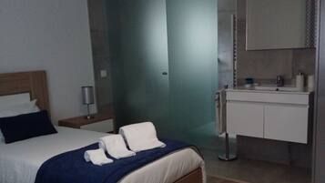 Une chambre d’hôtel avec un grand lit, une table de chevet, une lampe, une salle de bain avec un miroir et un lavabo.