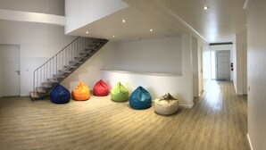 Un hall spacieux doté d’un plancher en bois, d’un escalier et de plusieurs fauteuils-pouf colorés disposés le long du mur.