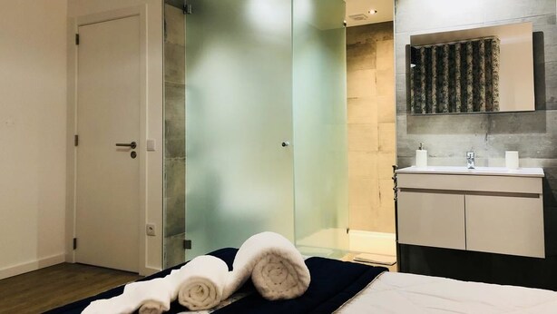 Une chambre d’hôtel moderne dotée d’une douche à parois de verre, d’un lit avec des serviettes pliées, d’un lavabo et d’un miroir au-dessus du comptoir.
