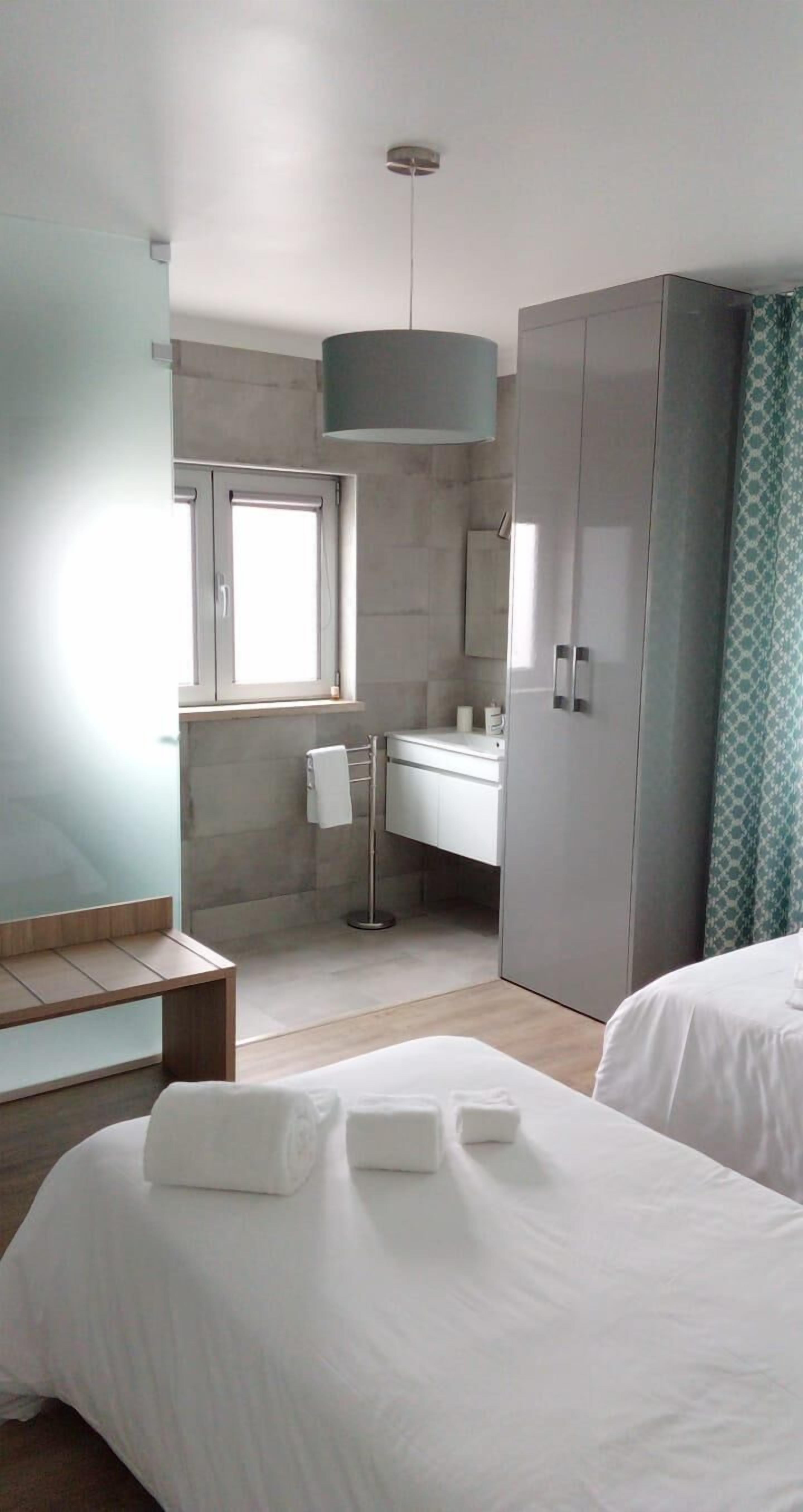 A modern hotel room with a large wardrobe, a bedside table, a bench, and a window.
