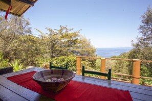A wooden deck with a red mat, a wicker basket with apples, and a view of the sea. - Appartamento Chalet Seccione (Portoferraio)
