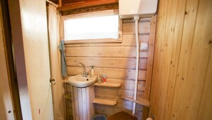 Et lille badeværelse med træpaneler, vask, toilet og vindue.