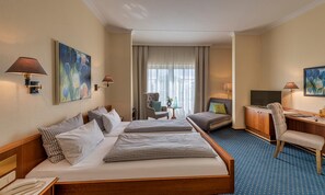 Quarto de hotel com duas camas, uma escrivaninha, uma cadeira, televisão e obras de arte nas paredes.
