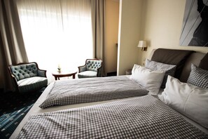 Habitación de hotel con una cama grande, dos sillones, una mesita y una lámpara.