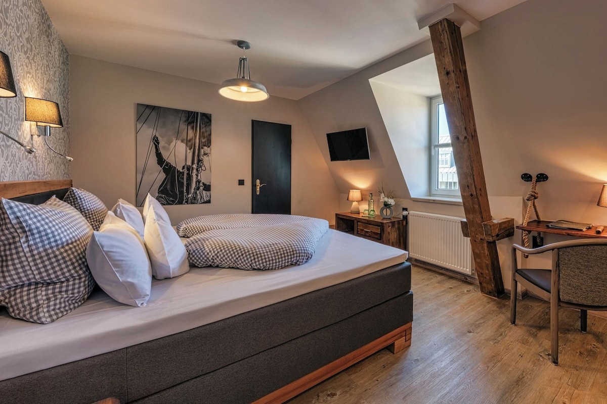 Un dormitorio con cama, escritorio, silla, ventana y un cuadro en la pared.