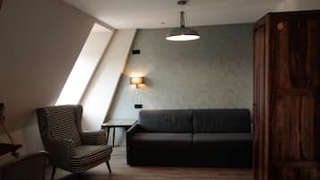 A loft-style room with a sloped ceiling, a black sofa, a checkered armchair, a small table, and a wall-mounted lamp.