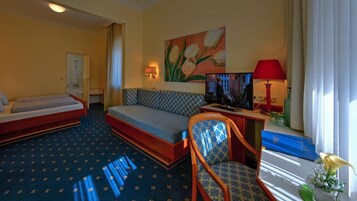 A hotel room with a bed, sofa, TV, and a painting on the wall.