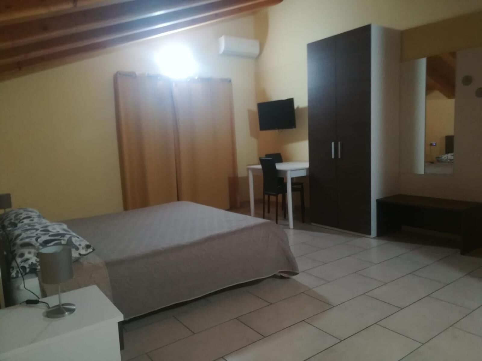 A bedroom with a bed, a desk, a chair, a wardrobe, and a television.