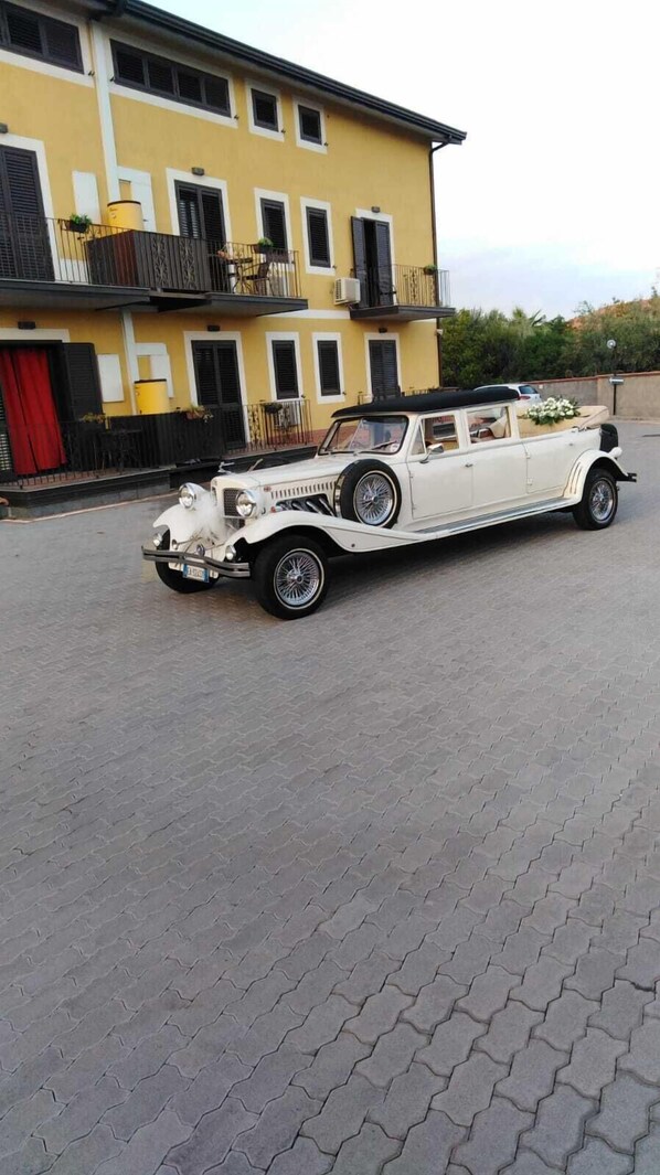 Une voiture décapotable blanche, modèle ancien, est garée devant un immeuble jaune doté de balcons.