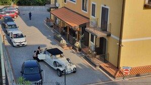 A street view with parked cars, a vintage car, and a building with a balcony.